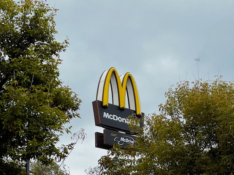 View of McDonald's sign surrounded by trees in Warsaw, Poland, under overcast sky.